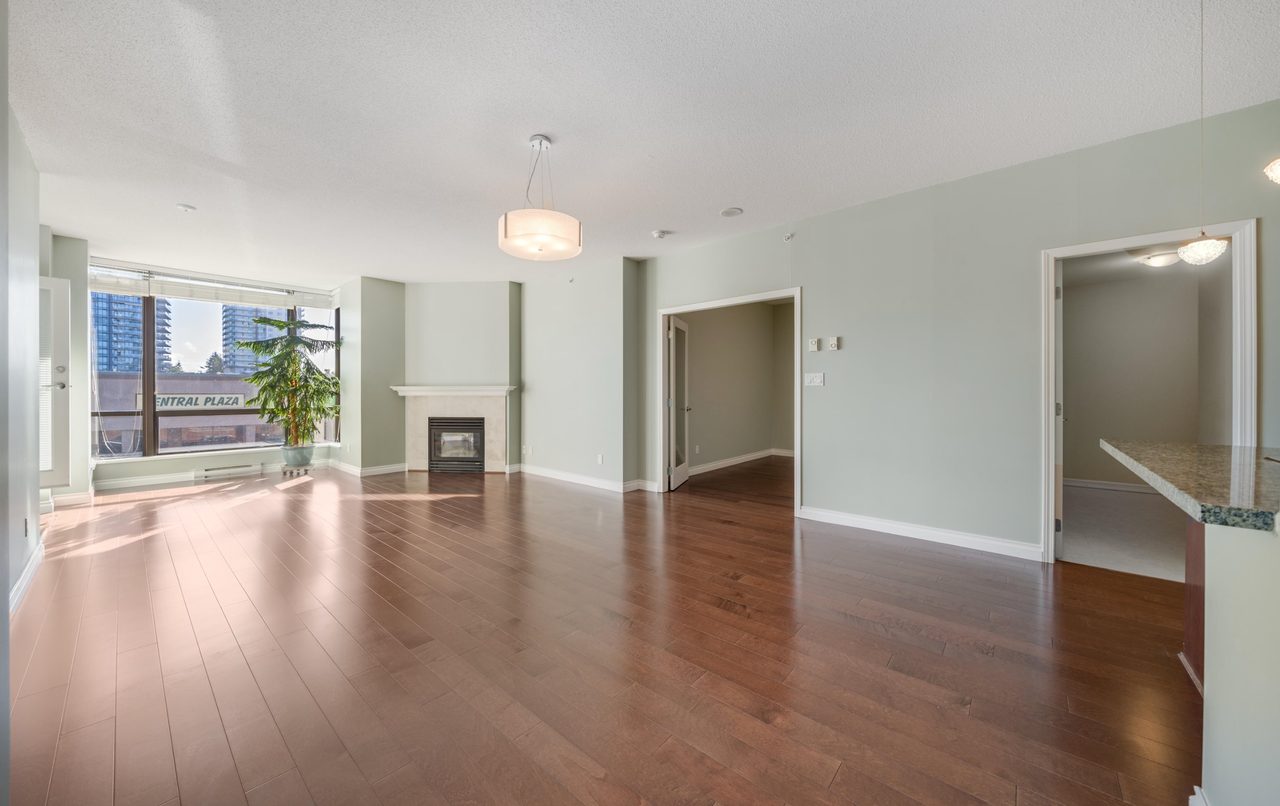 An empty condominium living room with hardwood floors, a fireplace and a corner window